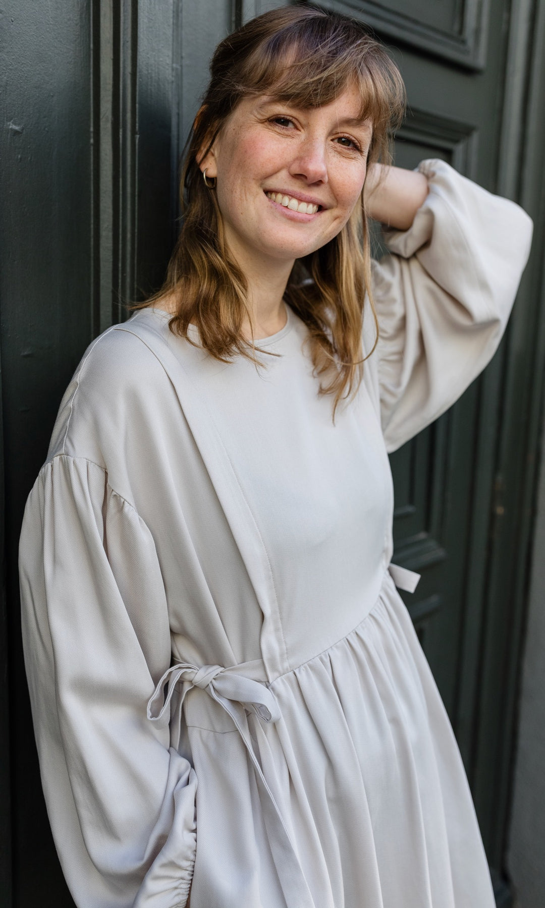 Stillkleid Shania in creme weiß als festliches Outfit für Hochzeit angelehnt an Tür Blick seitlich
