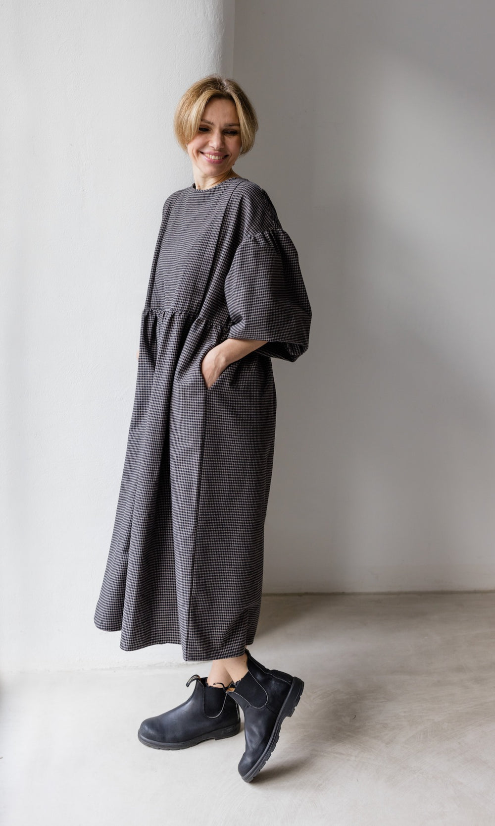 Winter Stillkleid Lovis in karo schwarz mit schwarzen Stiefeln seitlich Blick nach unten lächelnd