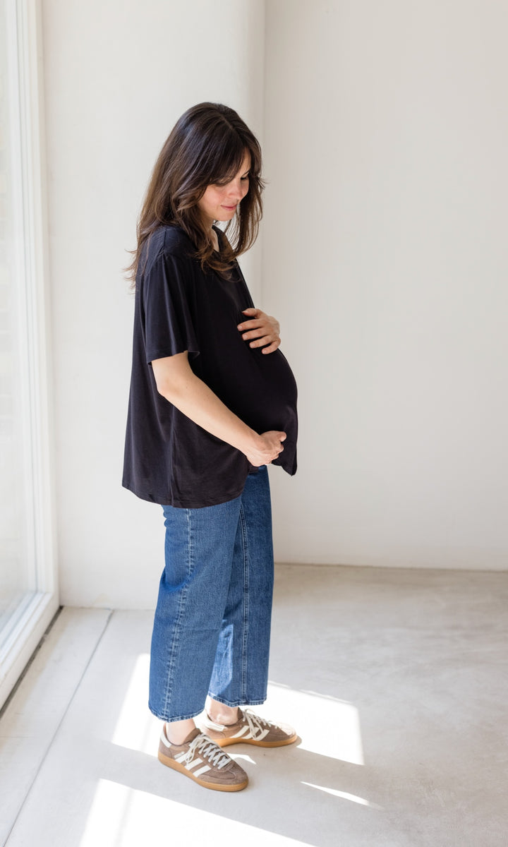 Schwangerschaftsjeans im French Fit Look in dunkelblau mit Bauchbund kombiniert mit schwarzem T-Shirt und braunen Sneakers. Blick nach unten.