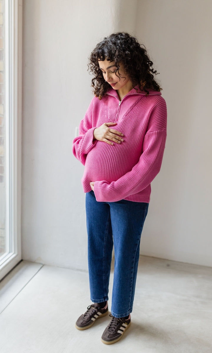 Schwangerschaftsjeans im French Fit Look in dunkelblau mit Bauchbund kombiniert mit rosa Strickpullover und braunen Sneakers. Blick auf Babybauch.
