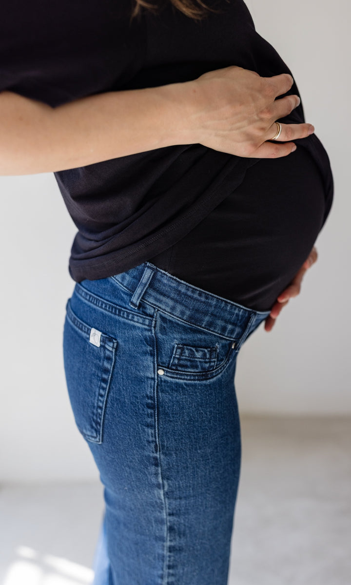 Schwangerschaftsjeans im French Fit Look in dunkelblau mit Bauchbund kombiniert mit schwarzem T-Shirt. Detailaufnahme Bauchbund.