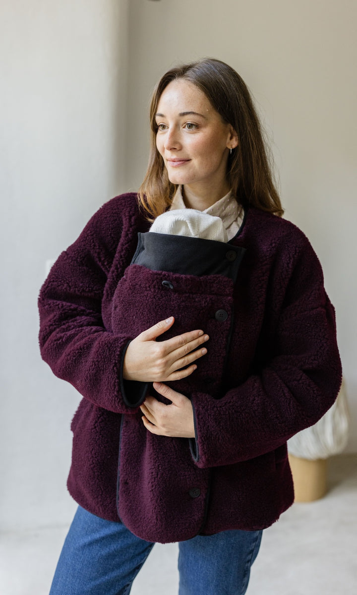 Babytrage Einsatz für Schafwoll Jacke in bordeaux rot mit blauer Jeans vor heller Wand Blick seitlich