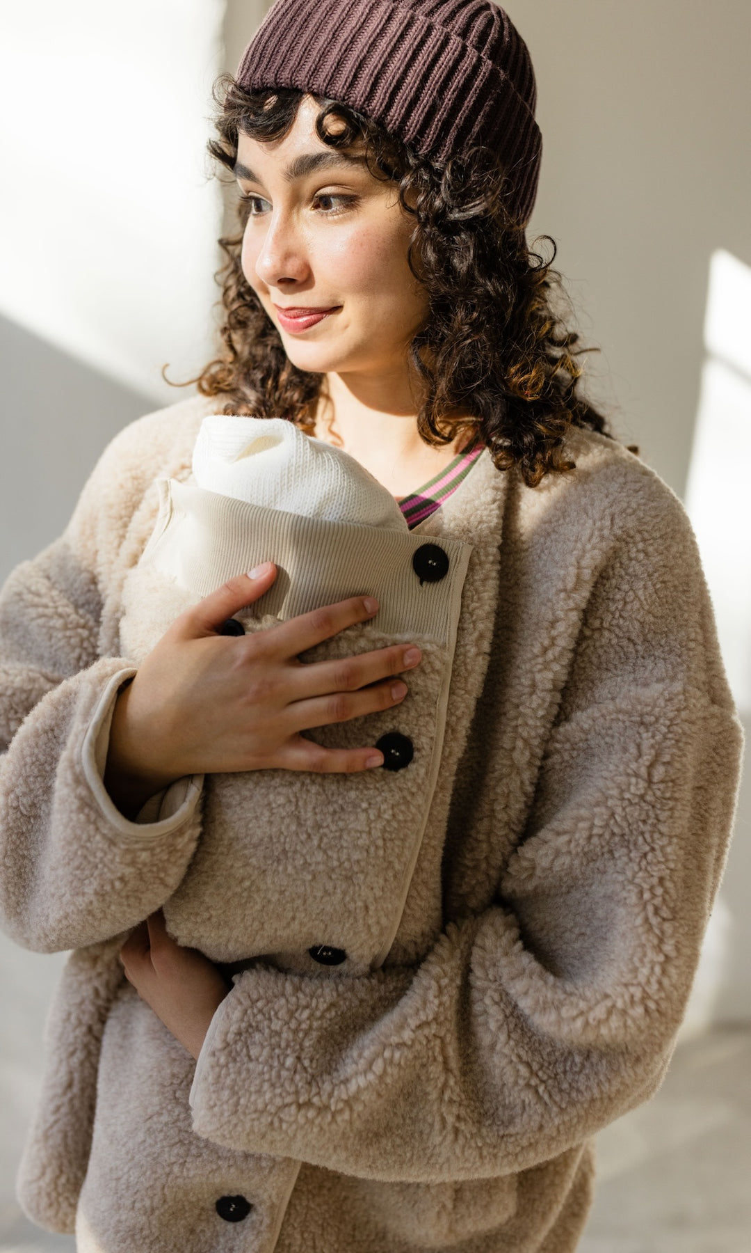 Babytrage Einsatz für Schafwoll Jacke in creme natur mit braunem Rock brauener Strickmütze vor heller Wand Blick seitlich