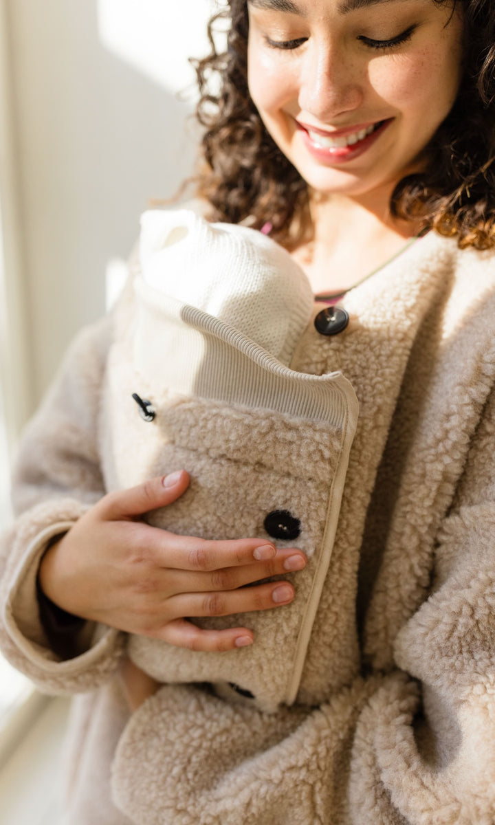 Babytrage Einsatz für Schafwoll Jacke in creme natur vor heller Wand Blick zum Kind lachend