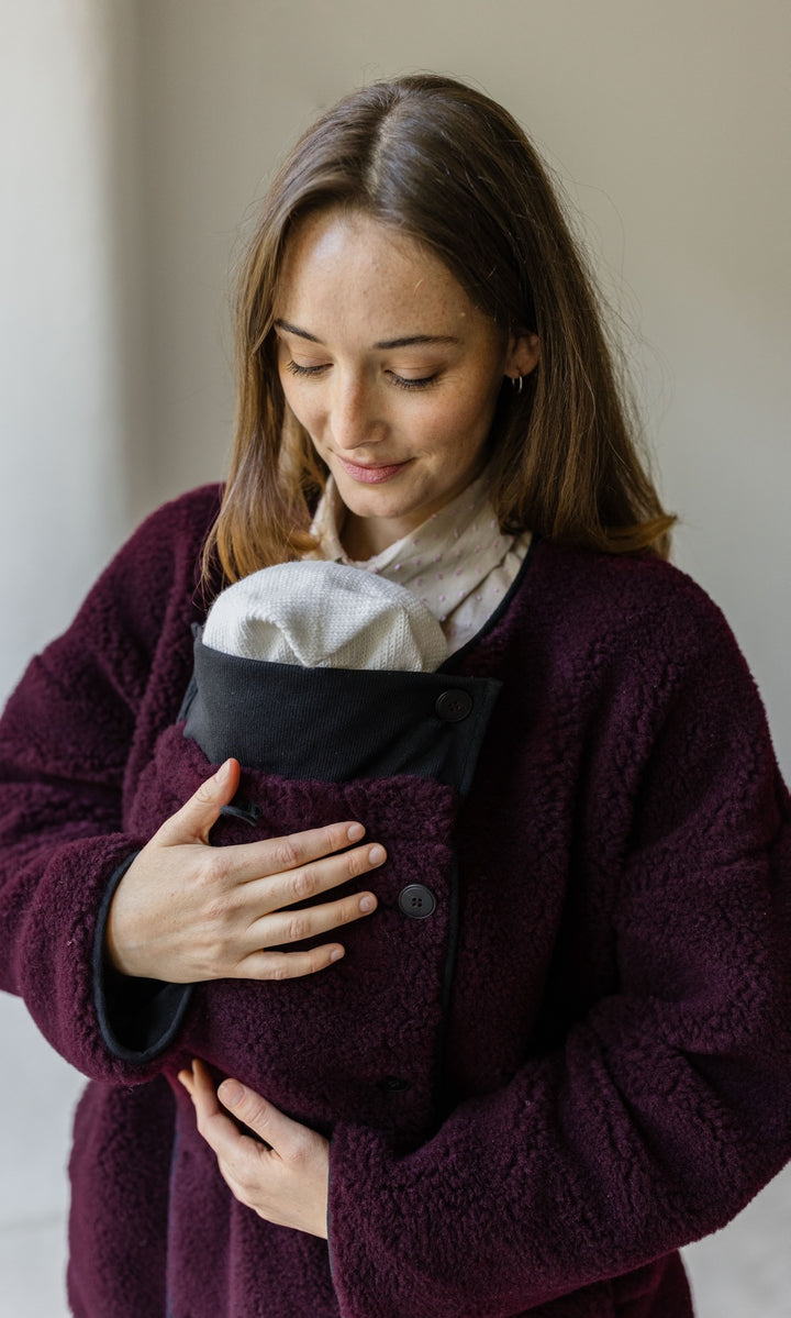 Babytrage Einsatz für Schafwoll Jacke in bordeaux rot vor heller Wand Blick zum Kind