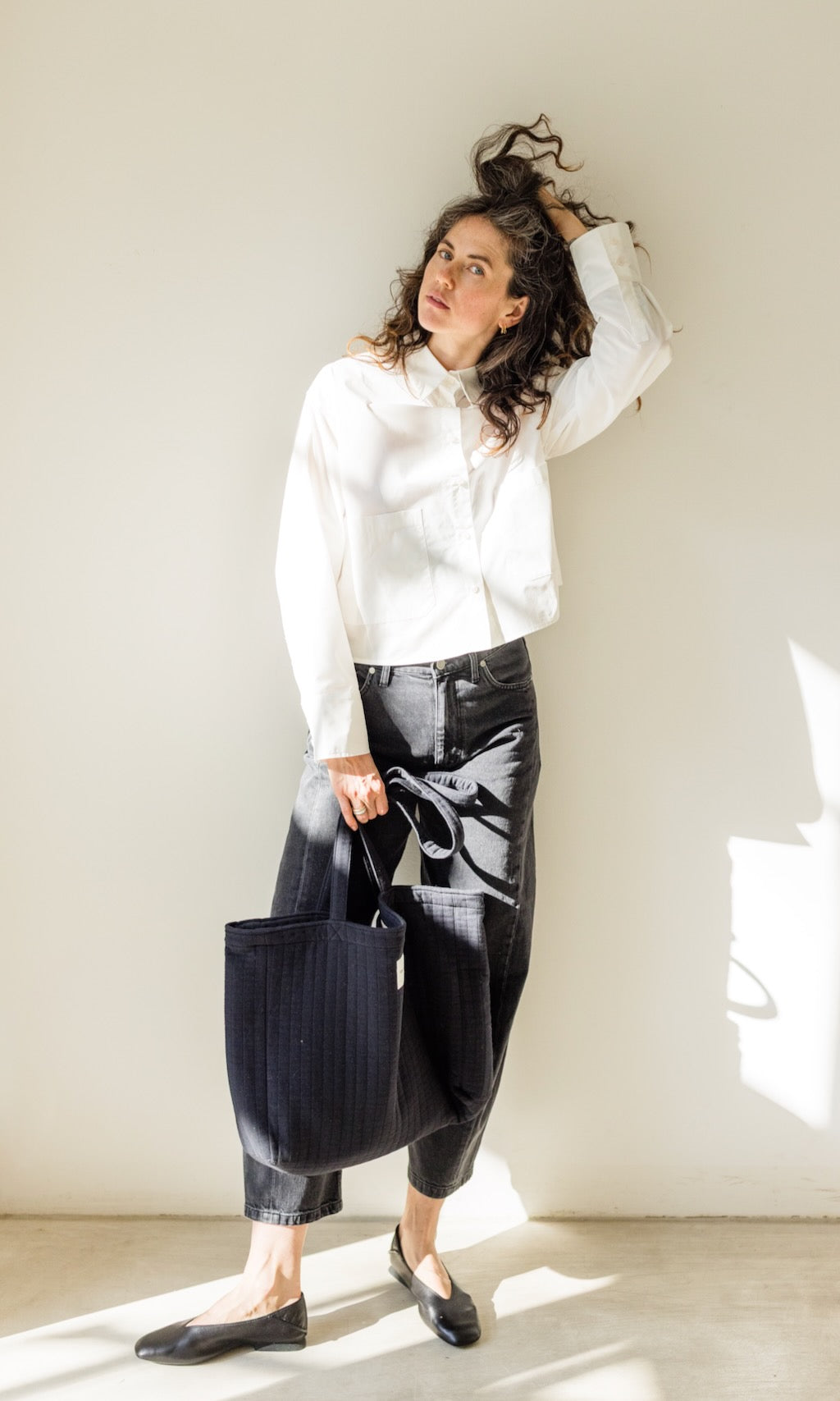 Das Modell trägt eine Barrel Jeans in schwarz kombiniert mit einem weißen Cropped Oversized Hemd und eleganten schwarzen Loafers für den Business-Look. Dazu eine große schwarze Tasche.