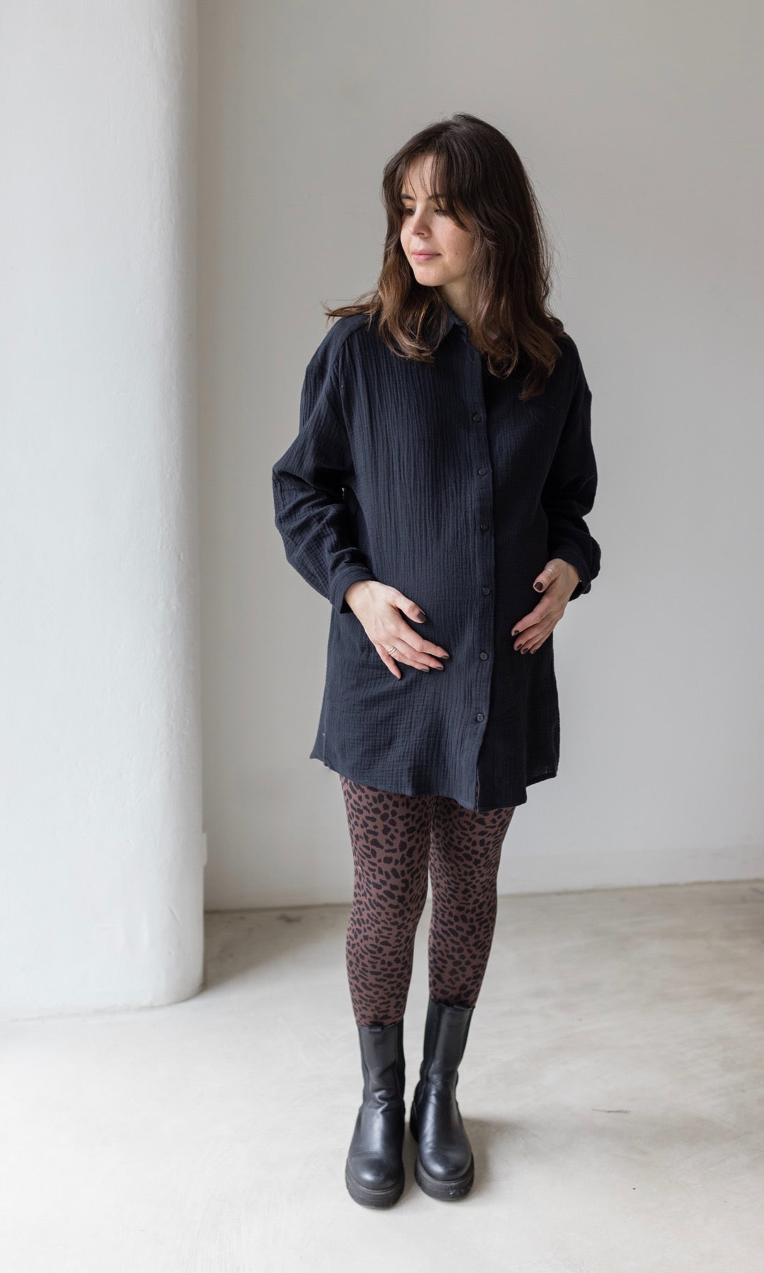 Braune Schwangerschaftsleggings leo Print mit schwarzem Musselin Hemd schwarzen Stiefeln seitlich vor heller Wand Blick seitlich