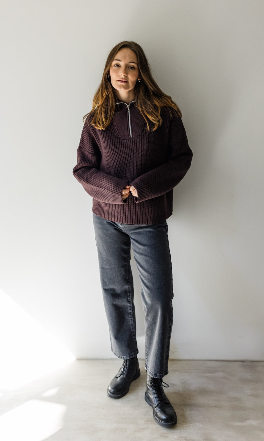 Gerippter Pullover mit Zipper Reissverschluss in braun mit dunkler Jeans und schwarzen Stiefeln vor heller Wand Blick gerade