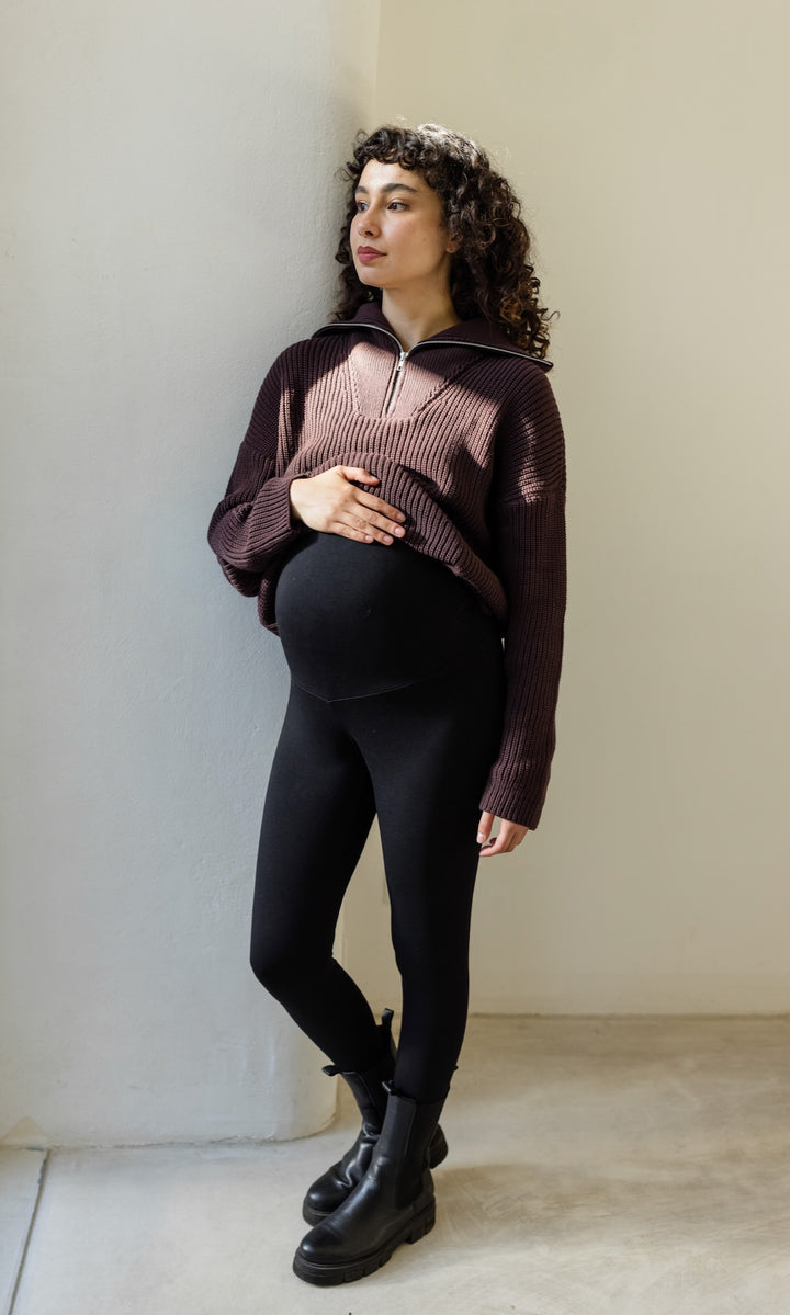 Gerippter Pulli mit Zipper Reissverschluss in braun mit schwarzer Umstandsleggings und schwarzen Stiefeln vor heller Wand Blick seitlich