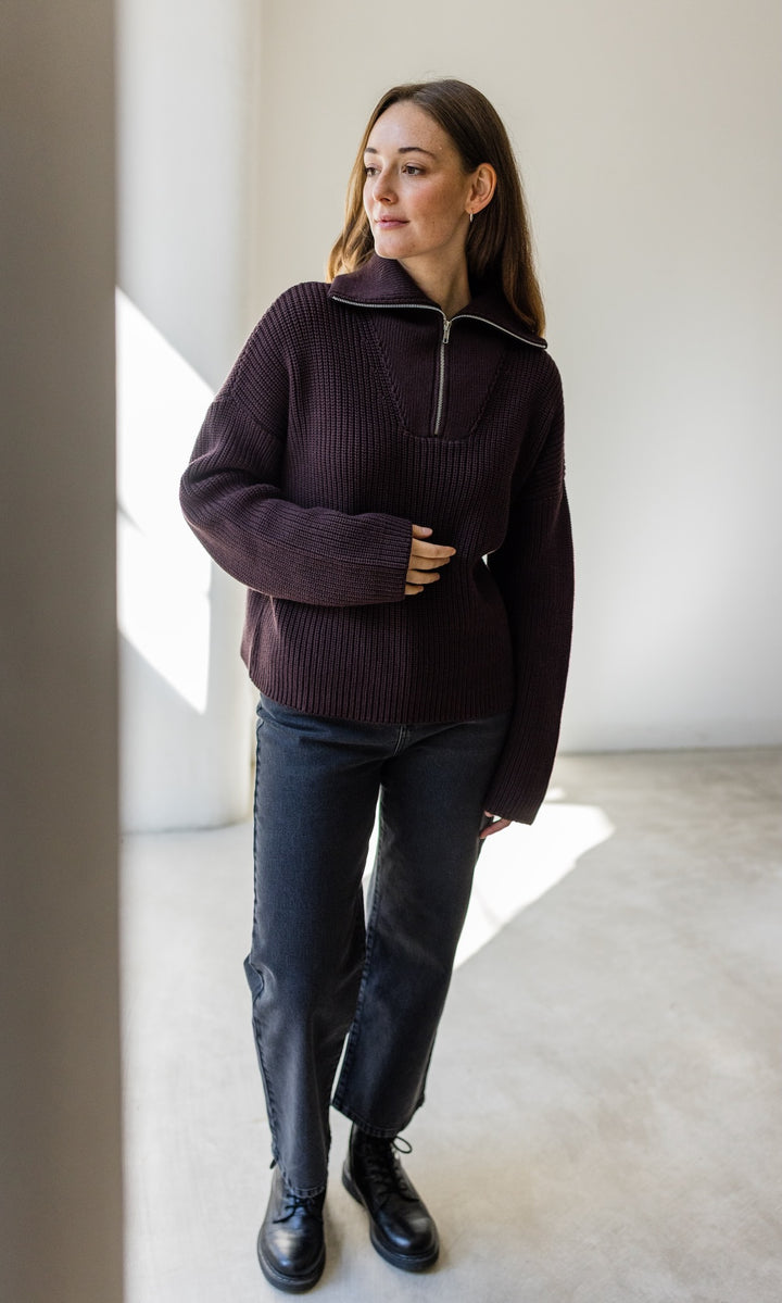Gerippter Pullover mit Zipper Reissverschluss in braun mit dunkler Jeans und schwarzen Schuhen vor heller Wand Blick seitlich