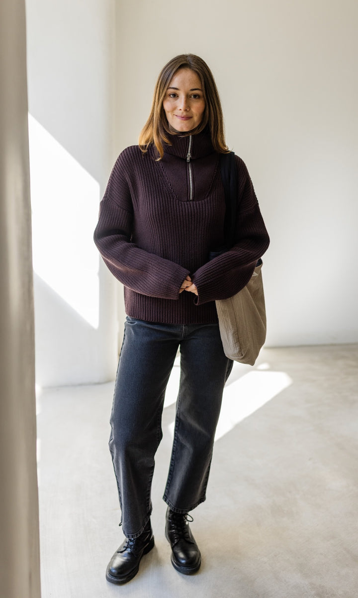 Gerippter Pullover mit Zipper Reissverschluss in braun mit dunkler Jeans, schwarzen Schuhen und weißer Shopper Bag vor heller Wand Blick gerade
