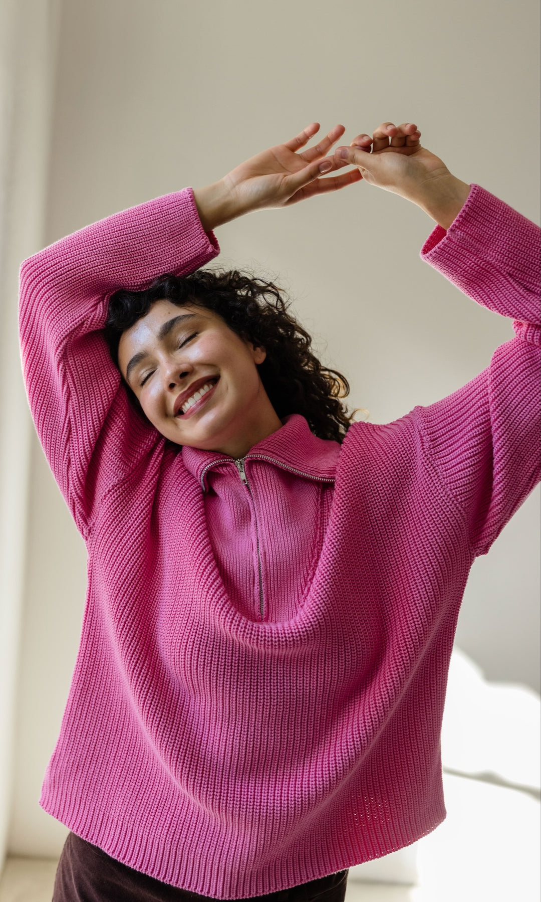 Gerippter Pullover mit Zipper Reissverschluss in rosa mit brauner Hose vor heller Wand lachend