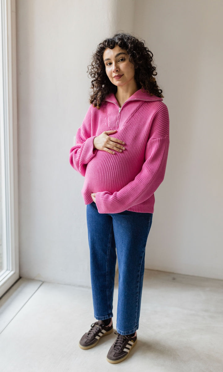 Gerippter Pullover mit Zipper Reissverschluss in rosa mit blauer Umstandsjeans und braunen Sneakers vor heller Wand