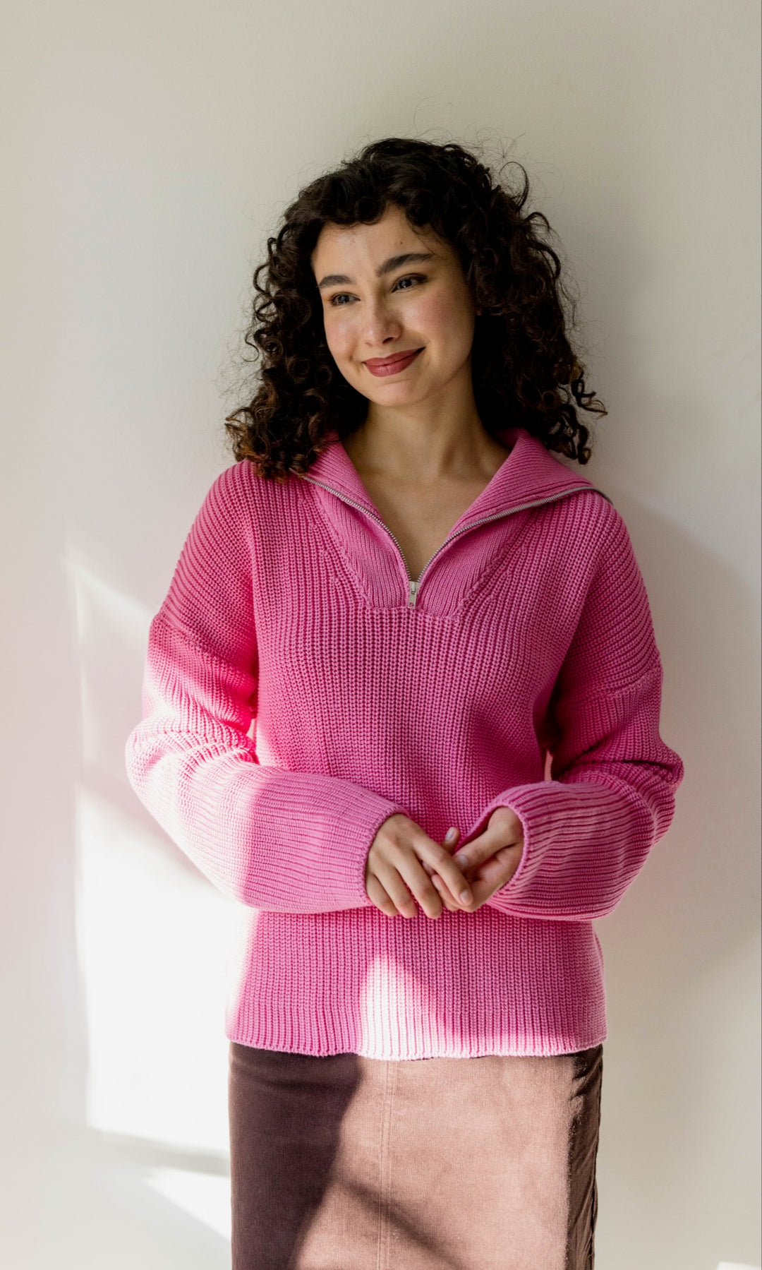 Gerippter Pullover mit Zipper Reissverschluss in rosa mit braunem Rock vor heller Wand Blick gerade