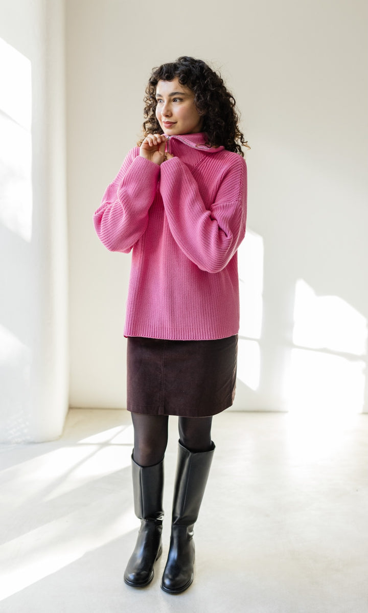 Gerippter Pullover mit Zipper Reissverschluss in rosa mit braunem Rock vor heller Wand Hand am Zipper