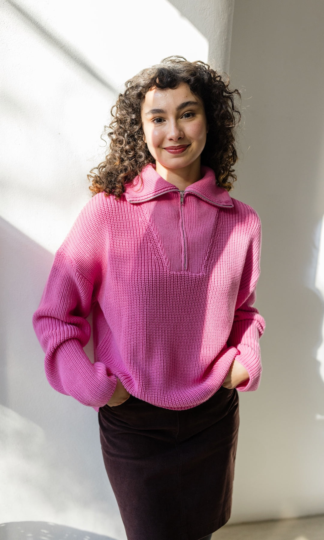 Gerippter Pullover mit Zipper Reissverschluss in rosa mit braunem Rock vor heller Wand Blick gerade