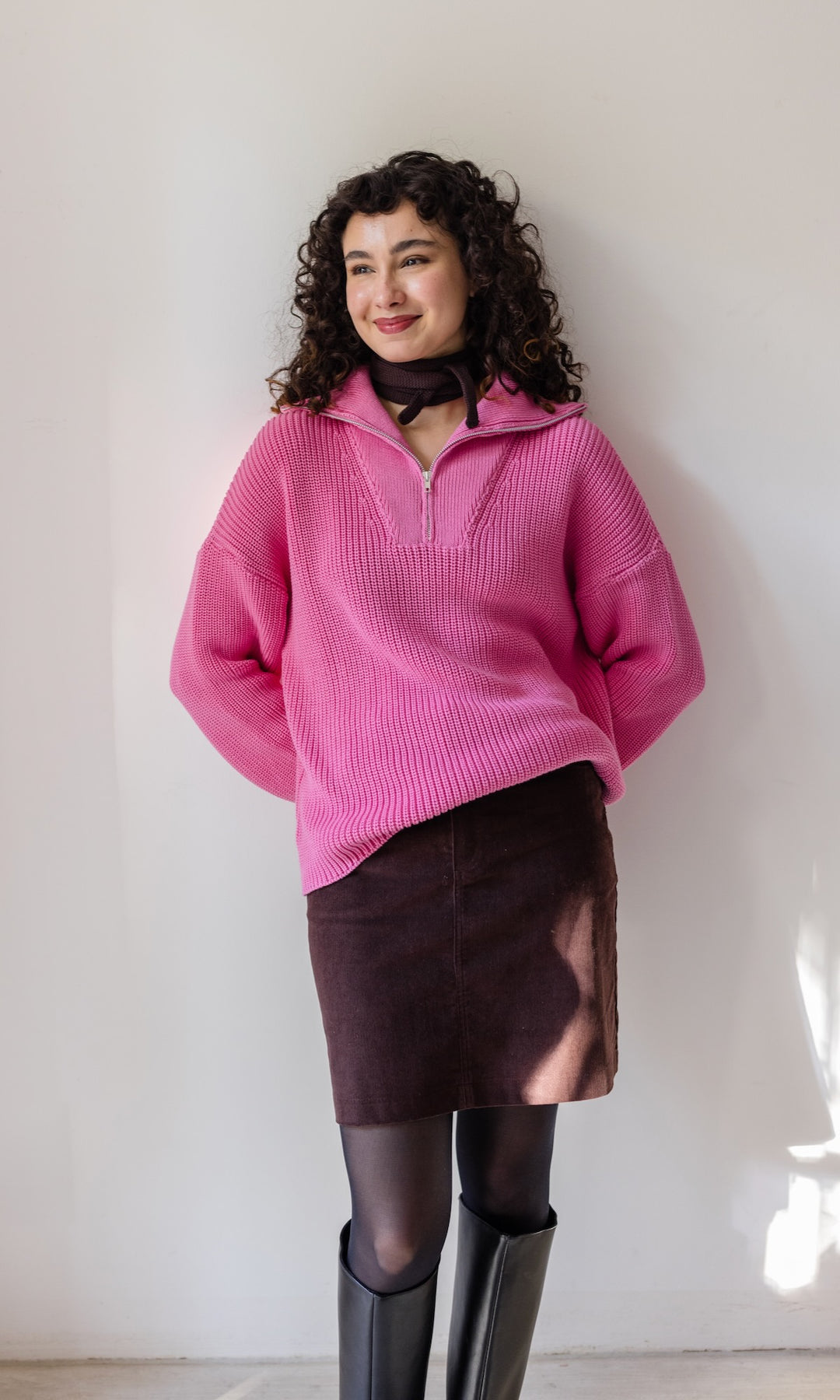 Gerippter Pullover mit Zipper Reissverschluss in rosa mit braunem Rock vor heller Wand Blick lächelnd aus Fenster