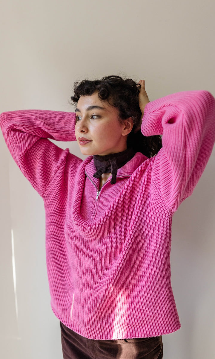 Gerippter Pullover mit Zipper Reissverschluss in rosa mit braunem Rock und kleinem Strickschal vor heller Wand Blick seitlich