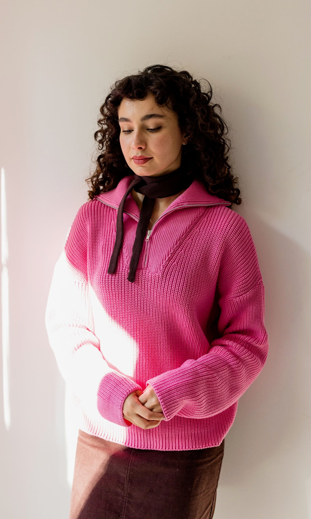 Gerippter Pullover mit Zipper Reissverschluss in rosa mit braunem Rock vor heller Wand Blick seitlich nach unten