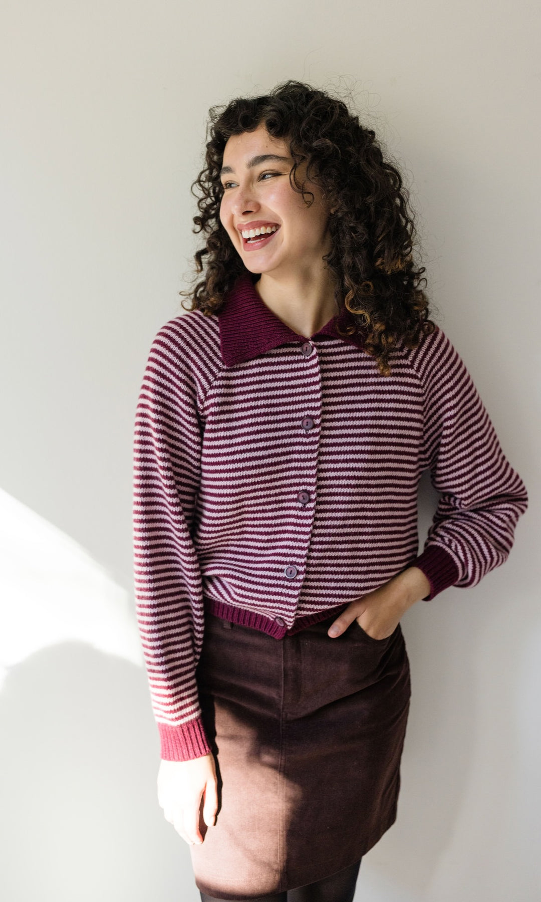 Gestreifte Strickjacke in rot weiß mit braunem Rock vor heller Wand Blick seitlich lachend
