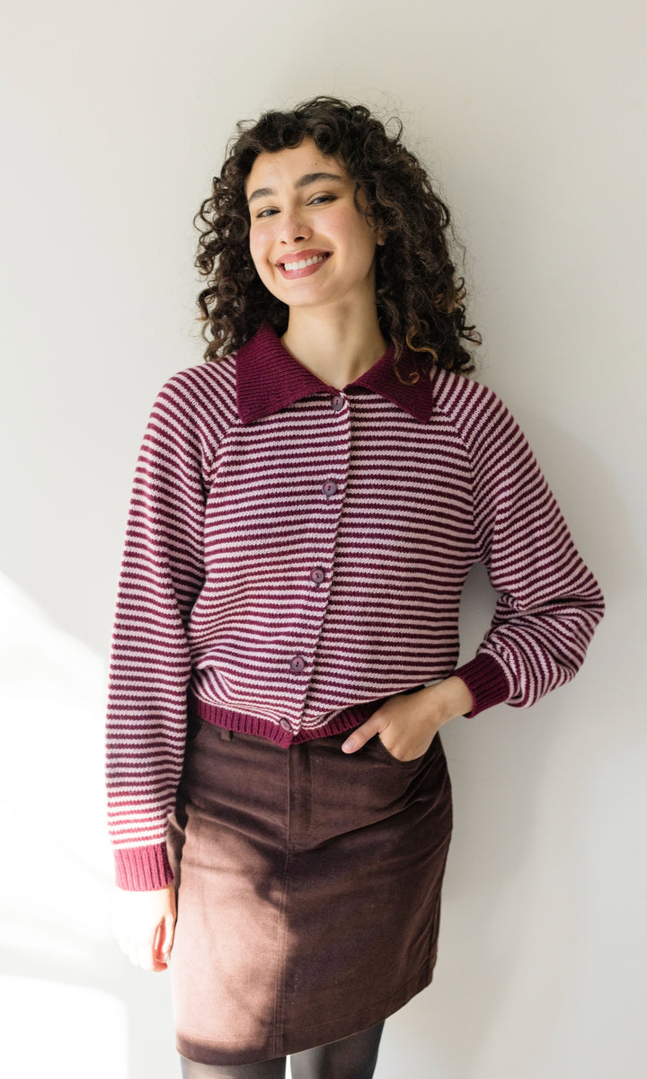 Gestreifte Strickjacke in rot weiß mit braunem Rock angelehnt an heller Wand Blick seitlich lachend