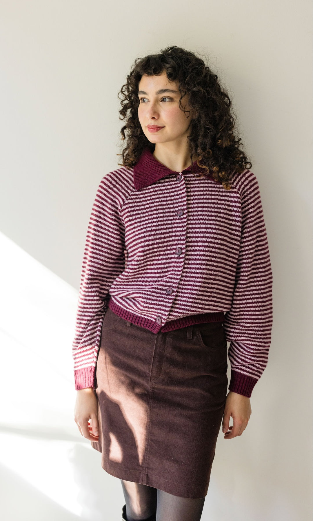 Gestreifte Strickjacke in rot weiß mit braunem Rock vor heller Wand Blick seitlich