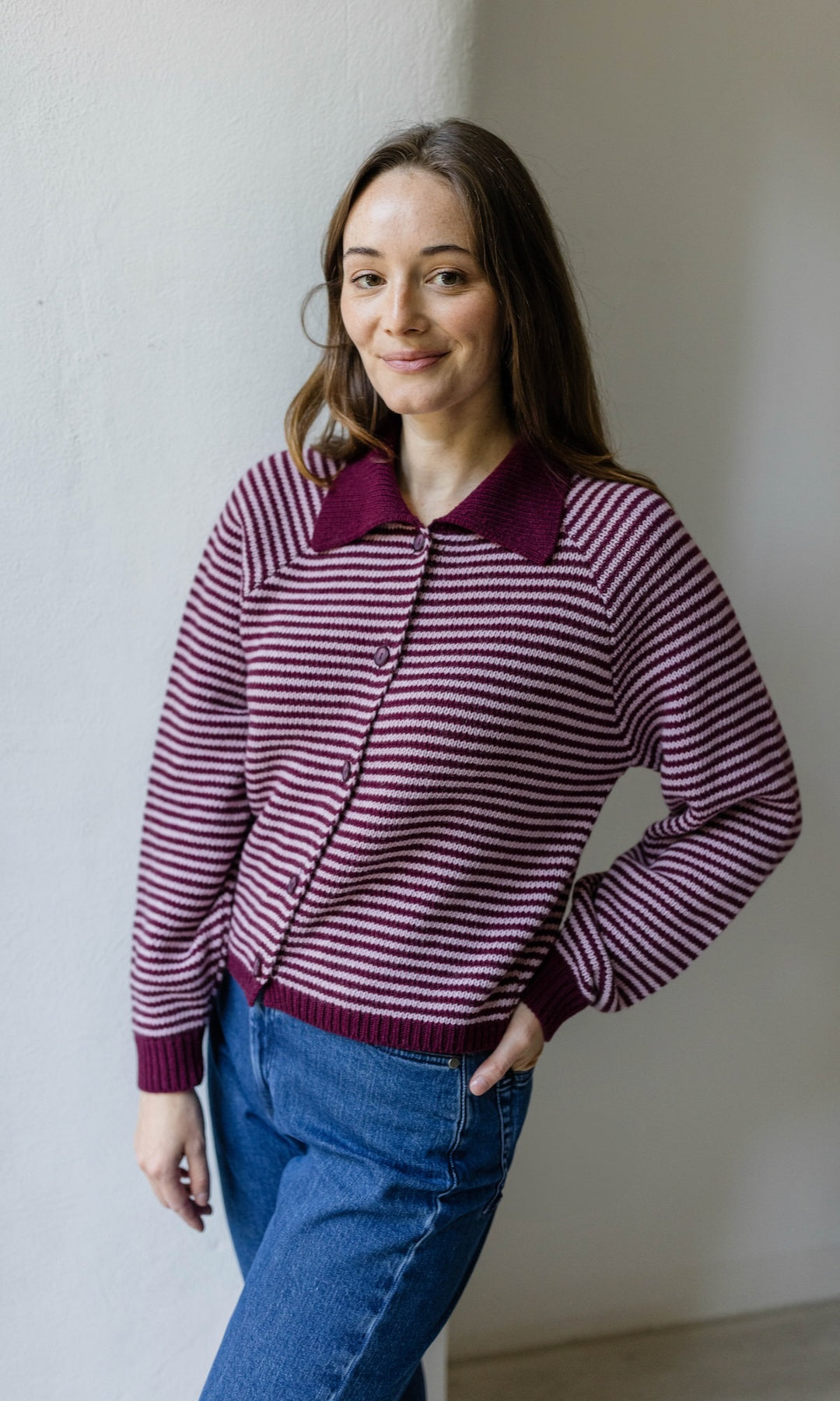 Gestreifte Strickjacke in rot weiß mit blauer Jeans vor heller Wand Blick gerade lächelnd