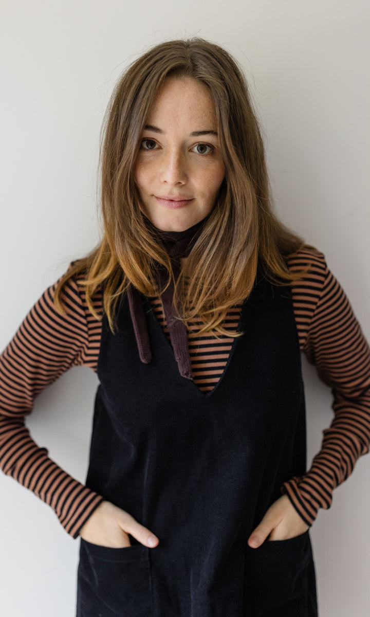 Kleiner Mini Strickschal in braun im Outfit mit braun gestreiftem Shirt, dunklem Kleid vor heller Wand Blick gerade