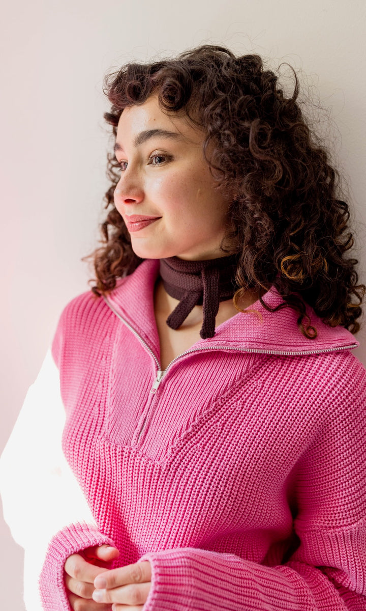 Kleiner Mini Strickschal in braun im Outfit mit Strick Pullover in pink vor heller Wand Blick seitlich