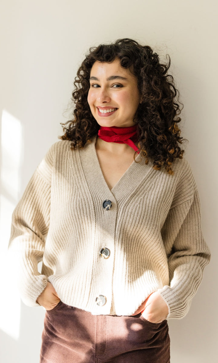 Kleiner Mini Strickschal in rot im Outfit mit hellem Strick Cardigan, braunem Rock vor heller Wand Blick gerade lächelnd