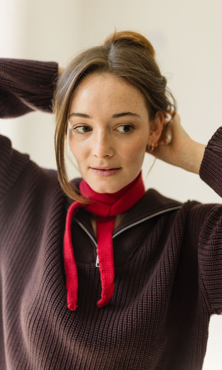 Kleiner Mini Strickschal in rot im Outfit mit rotem Pullover vor heller Wand Blick gerade