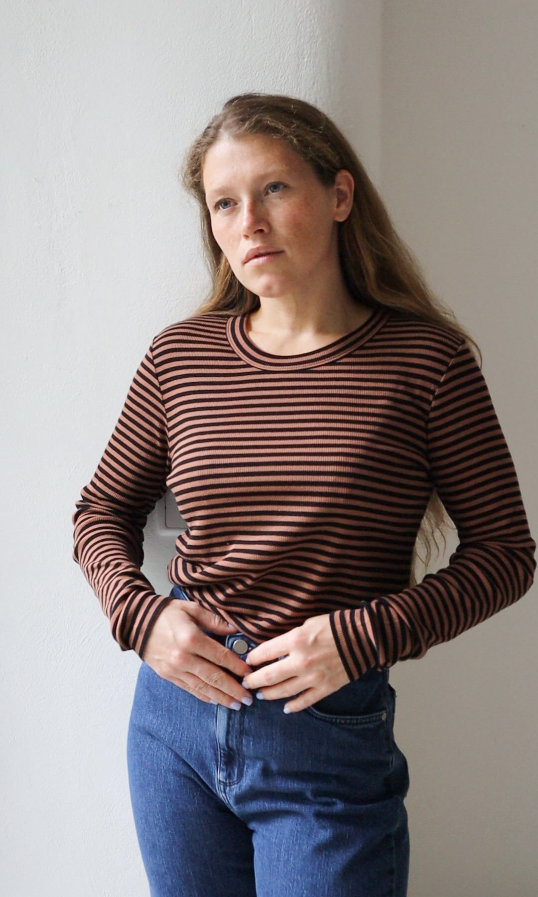 Langarm Stillshirt Zoe in braun gestreift kombiniert mit blauer Jeans vor grauer Wand von vorne Blick seitlich
