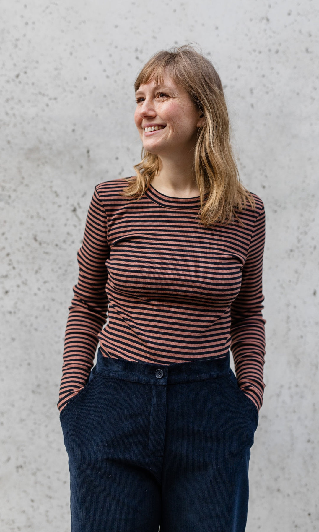 Langarm Stillshirt Zoe in braun gestreift kombiniert mit schwarzer Hose vor grauer Wand im Herbst von vorne Blick seitlich