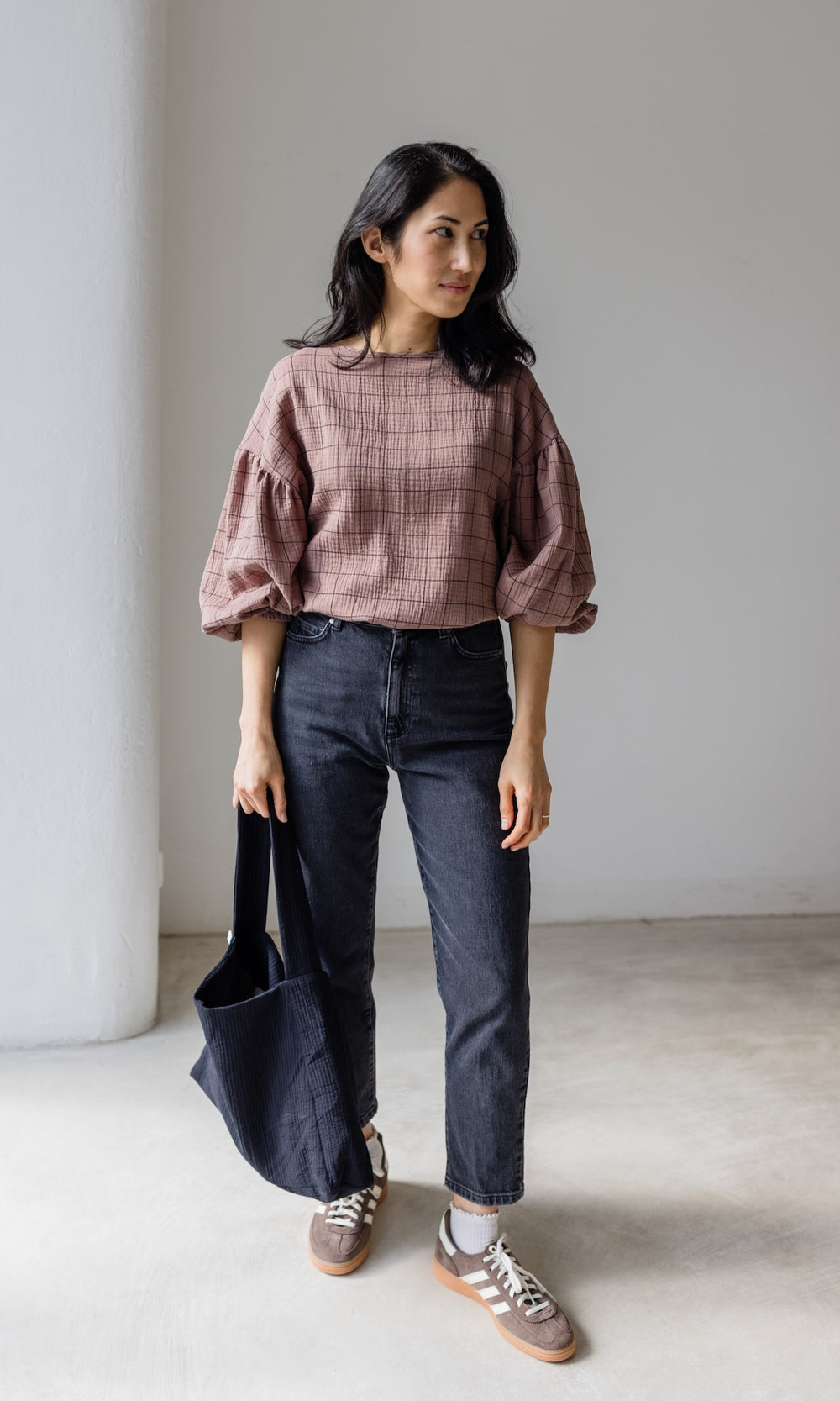Mom Fit Jeans in schwarz aus Bio-Baumwolle kombiniert mit brauner Musselin-Bluse, braunen Sneakers und schwarzer Mom Bag für einen lässig-schicken Look.