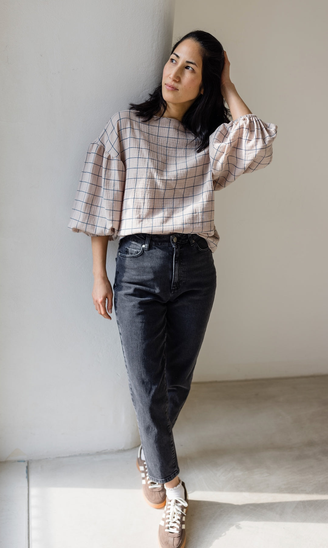 Mom Fit Jeans in schwarz aus Bio-Baumwolle kombiniert mit creme-farbener Musselin-Bluse und braunen Sneakers für den schicken Look.