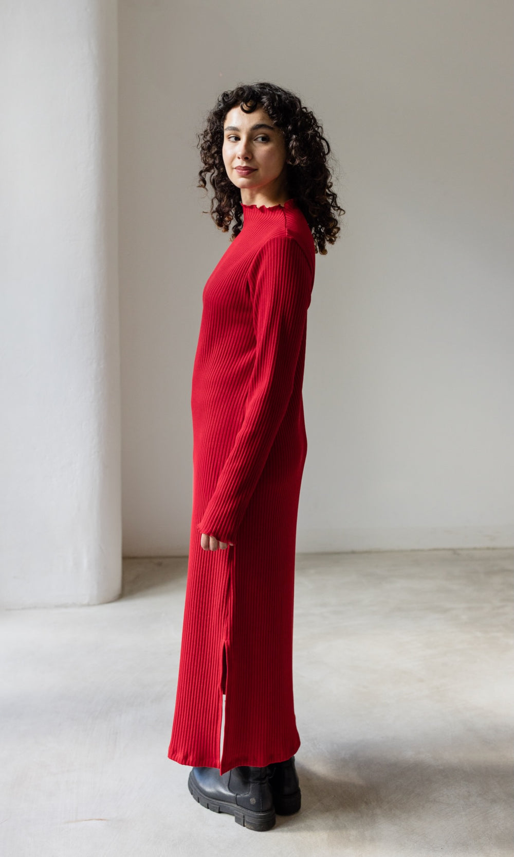 Rotes Strickkleid Jil lang in langarm mit schwarzen Stiefeln seitlich stehend Blick seitlich