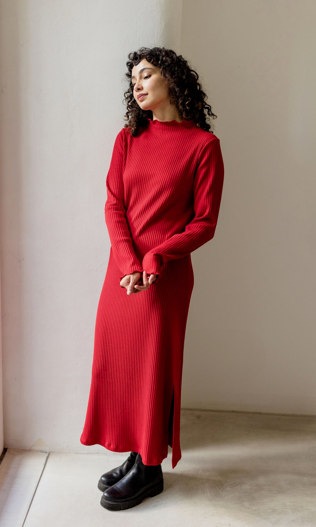 Rotes Strickkleid Jil langarm mit schwarzen Stiefeln als Outfit für Weihnachten seitlich stehend Kopf geneigt.