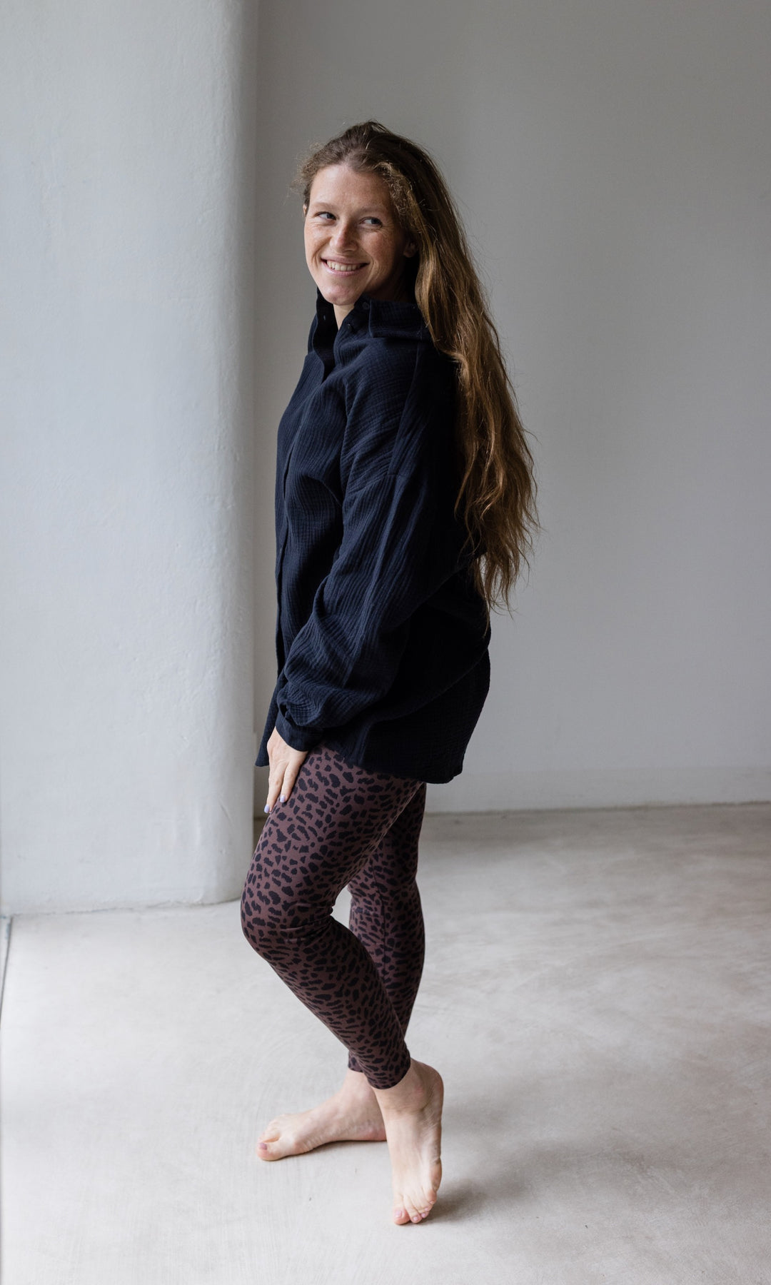 Schwangerschaftsleggings braun leo Print mit schwarzem Musselin Hemd seitlich vor heller Wand Blick nach vorne lächelnd