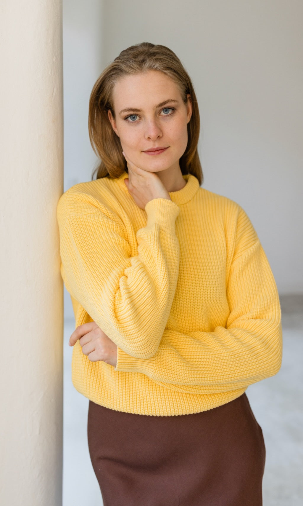 Senfgelber Strickpullover aus Bio-Baumwolle kombiniert mit braunem Rock als schickes Business-Outfit.