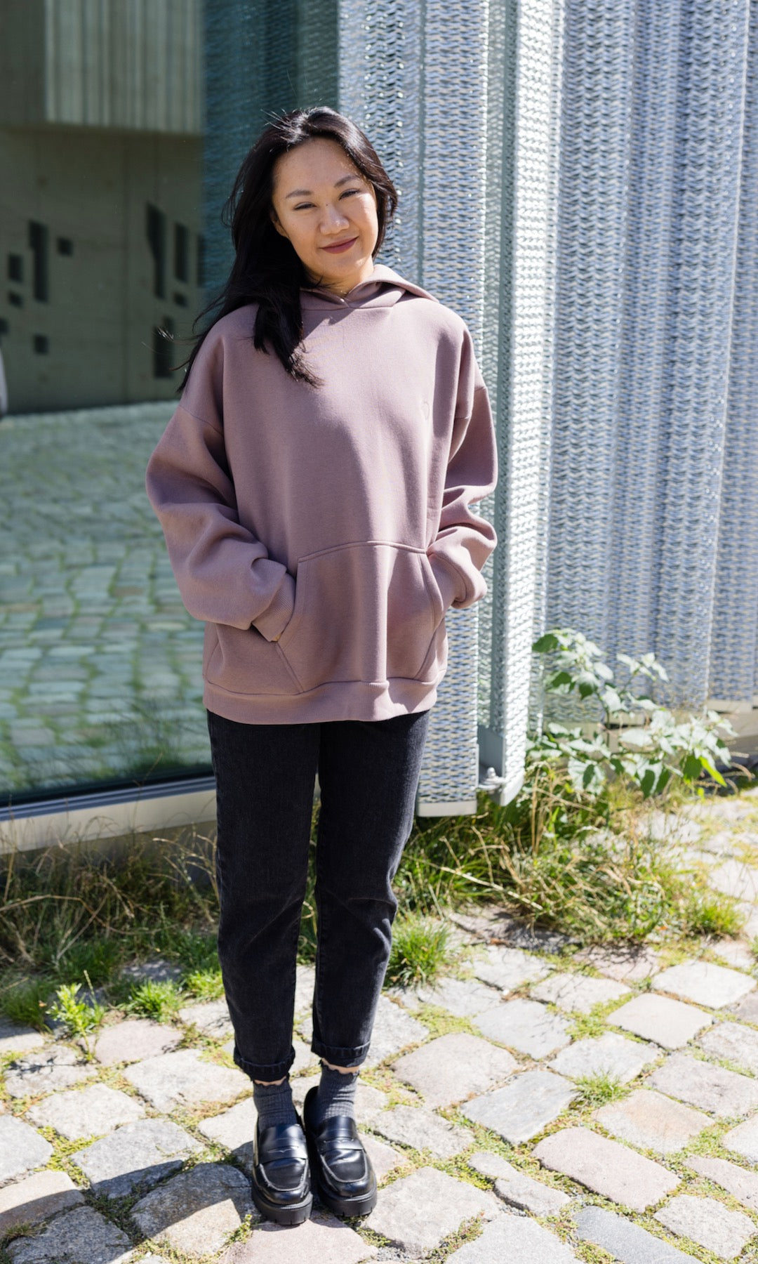 Still Hoodie in aubergine rot stehend mit schwarzer Hose und Stiefeln vor Fenster Hände in Tasche von vorne Blick gerade 