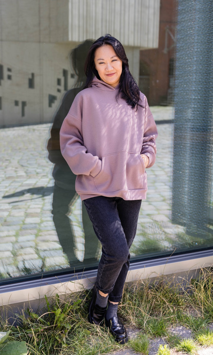 Still Hoodie in aubergine rot stehend mit schwarzer Hose und Stiefeln angelehnt an Fensterscheibe Hände in Tasche von vorne