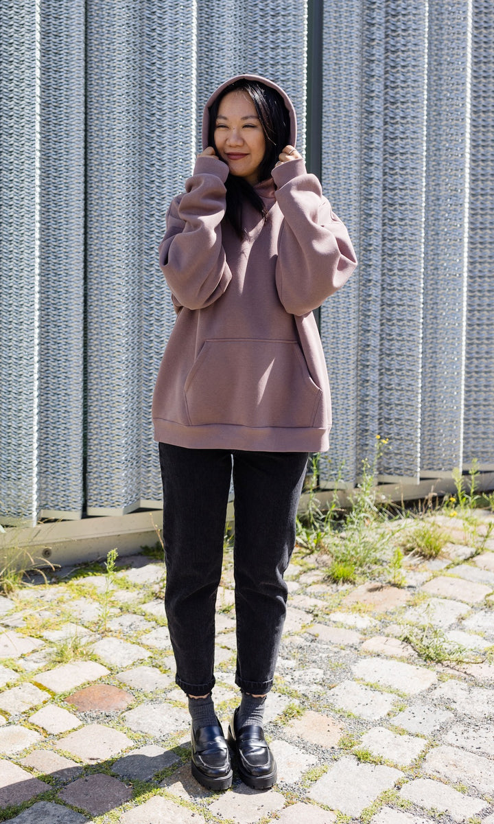 Still Hoodie in aubergine rot stehend mit schwarzer Hose und Stiefeln vor grauer Wand Kapuze auf Kopf von vorne Blick gerade 