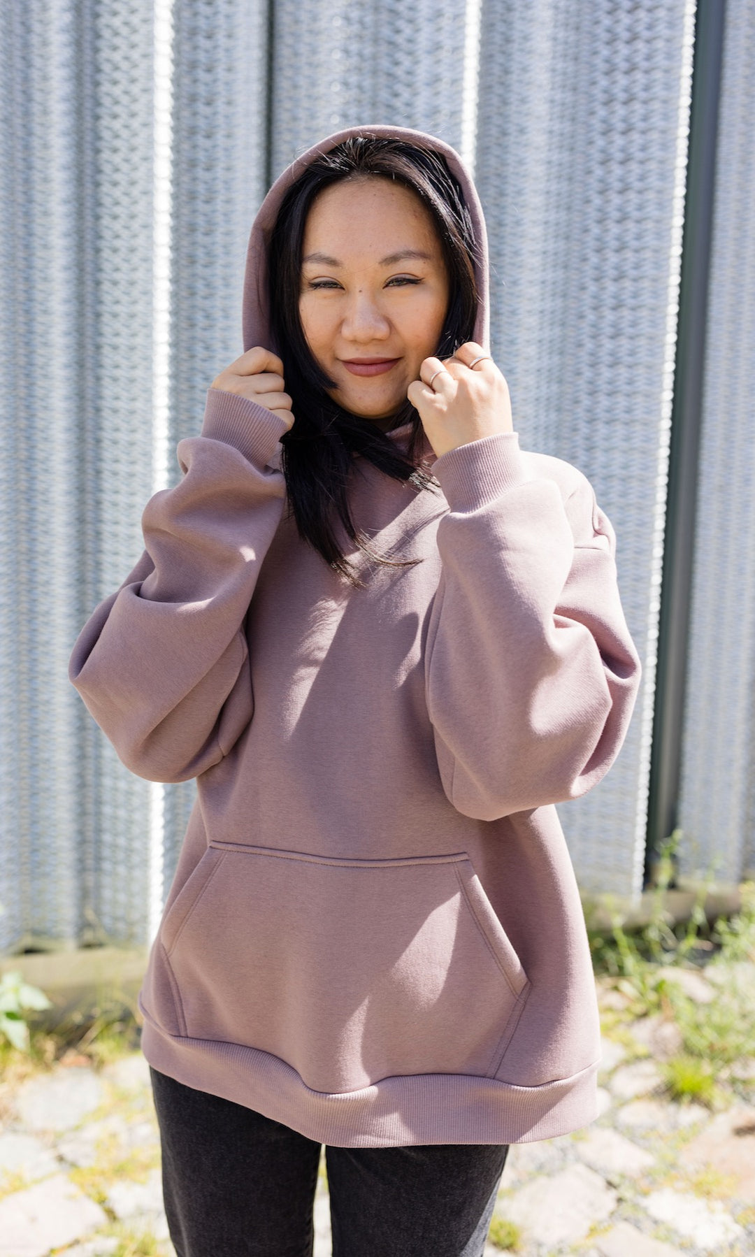 Still Hoodie in aubergine rot stehend mit schwarzer Hose Kapuze auf Kopf vor grauer Wand Nahaufnahme von vorne