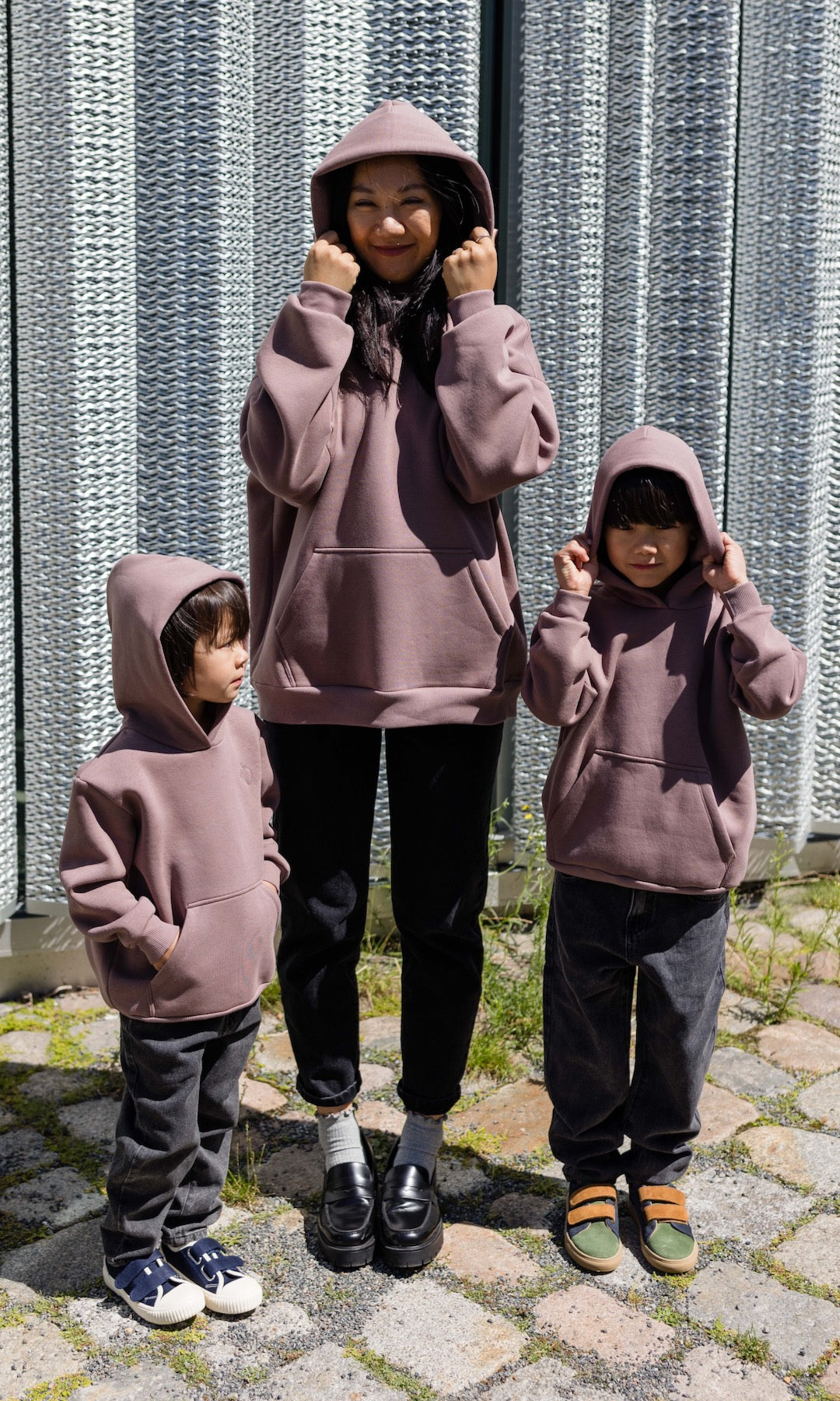 Still Hoodie in aubergine rot stehend mit Frau und zwei Kindern alle mit Still-Hoodie Kapuze auf Kopf Blick nach vorne