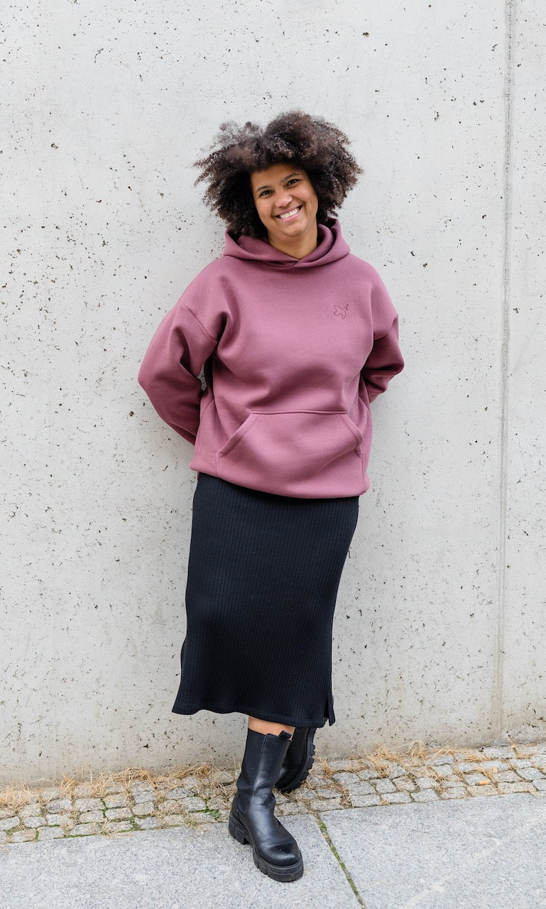 Still Hoodie in feige rosa vor grauer Wand kombiniert mit schwarzem Rock und Stiefeln im Herbst von vorne Blick gerade lächelnd