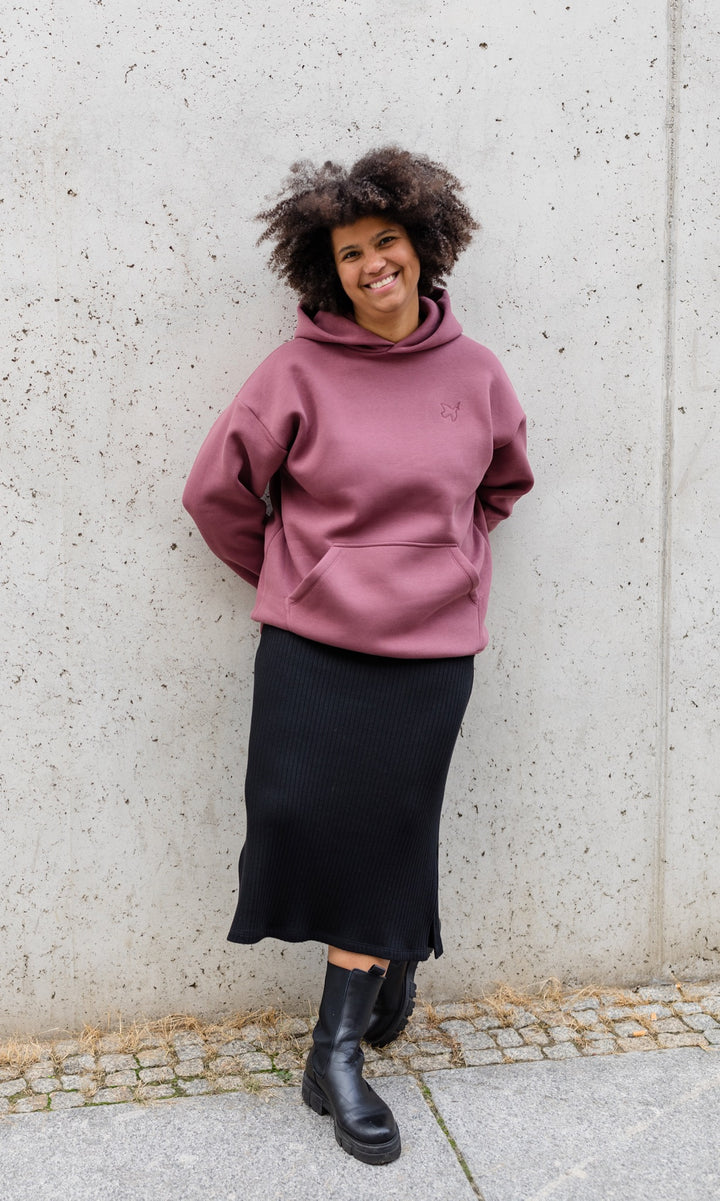 Still Hoodie in feige rosa vor grauer Wand kombiniert mit schwarzem Rock und Stiefeln im Herbst von vorne Blick gerade lachend