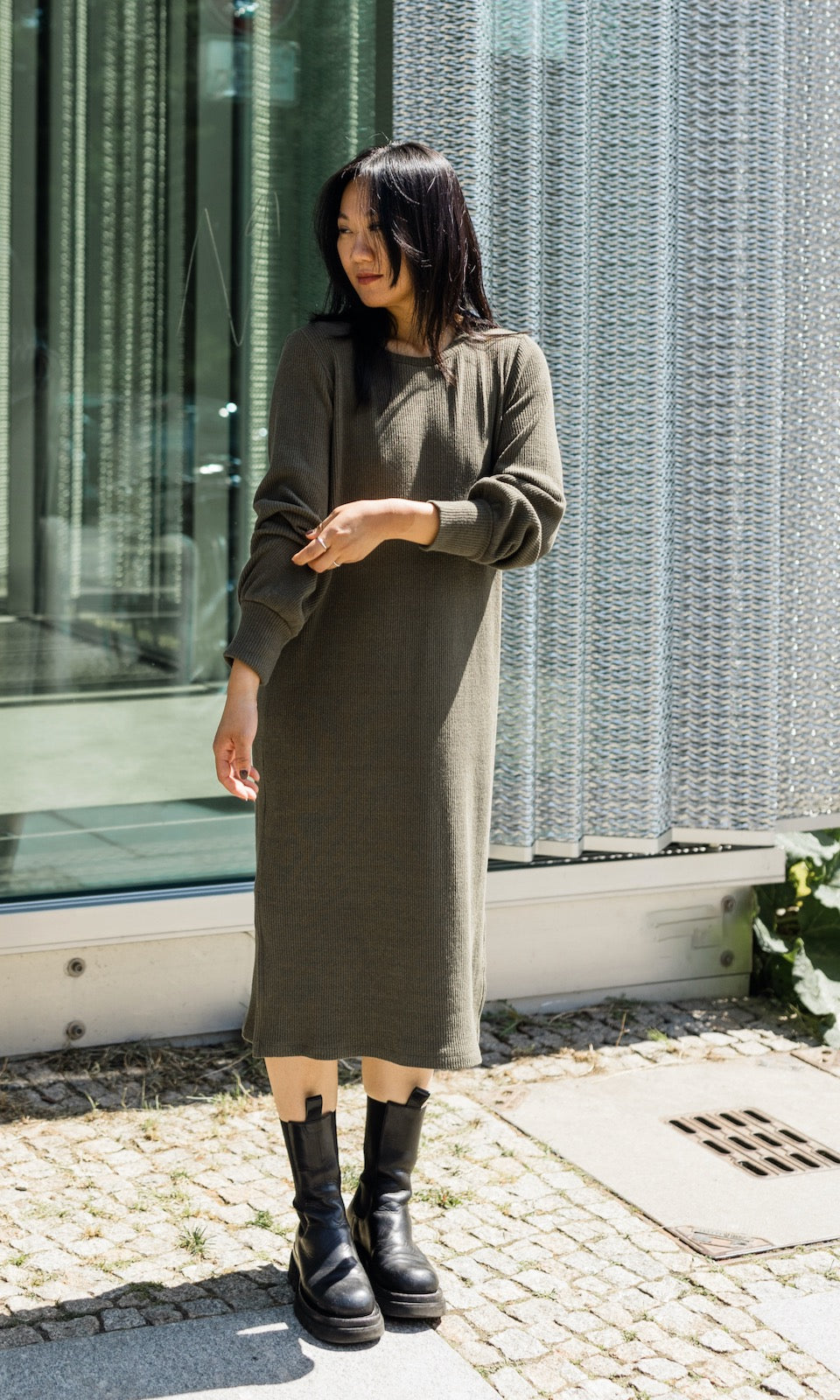 Still Strickkleid Jules in grün olive im festlichen Look mit Stiefeln frontal vor Fenster Blick seitlich