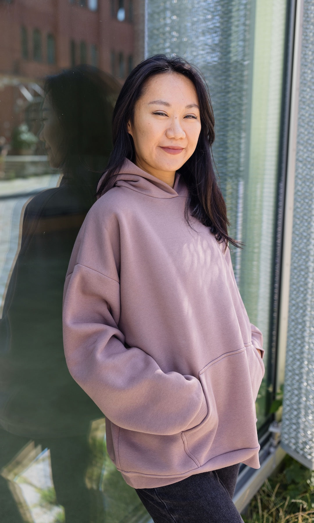 Still Sweatshirt in aubergine rot lässig stehend an Glasscheibe Hände in Tasche seitlich