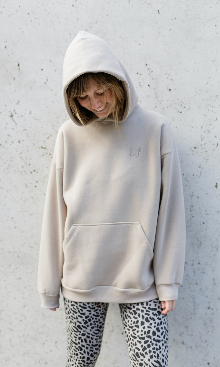 Stillhoodie in sesam weiß stehend im Herbst mit Leo Leggings vor grauer Wand Kapuze auf Kopf von vorne Blick nach unten