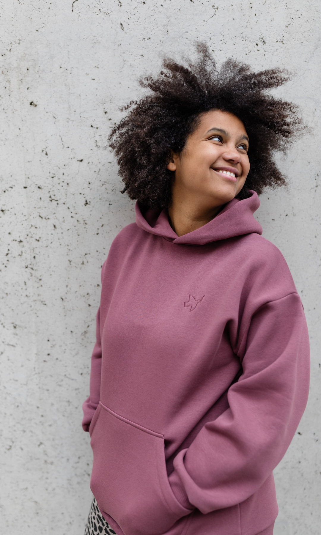 Stillhoodie in feige rosa vor grauer Wand seitlich Blick nach oben lächeln